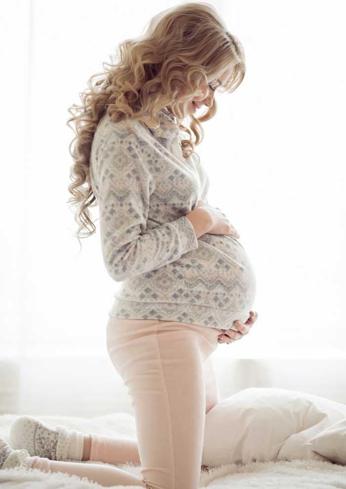 Schwangere-kniet-Aufrecht-in-Bett-und-haelt-Babybauch