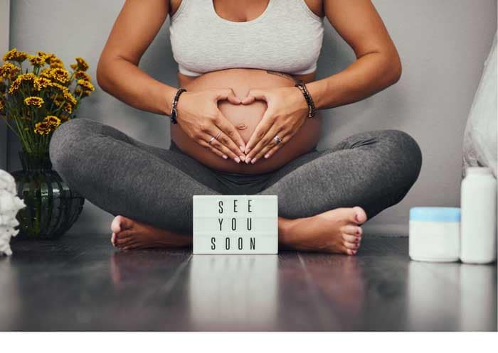 Schwangere-sitzt-im-Schneidersitz-mit-Schild-See-you-soon